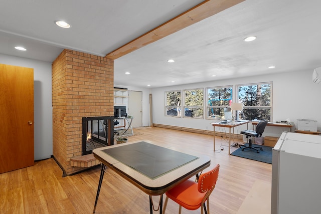 interior space featuring a brick fireplace, beam ceiling, a wall mounted air conditioner, and light wood-type flooring