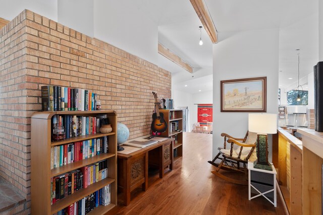 sitting room with hardwood / wood-style floors, beam ceiling, and brick wall