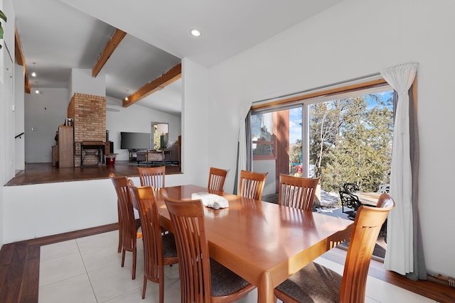 dining area with light tile patterned flooring, a brick fireplace, and vaulted ceiling with beams