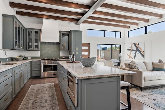 kitchen with premium range hood, a center island with sink, gray cabinets, a breakfast bar area, and appliances with stainless steel finishes