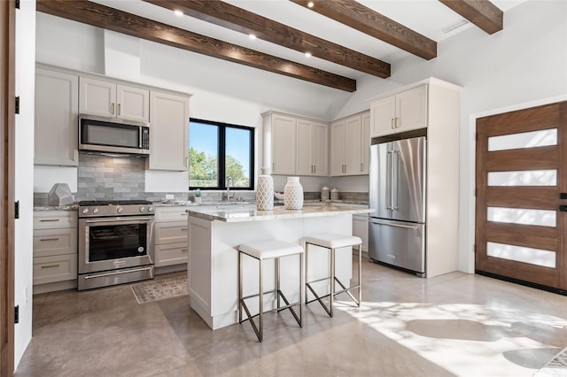 kitchen with appliances with stainless steel finishes, a kitchen island, a kitchen breakfast bar, light stone counters, and beam ceiling