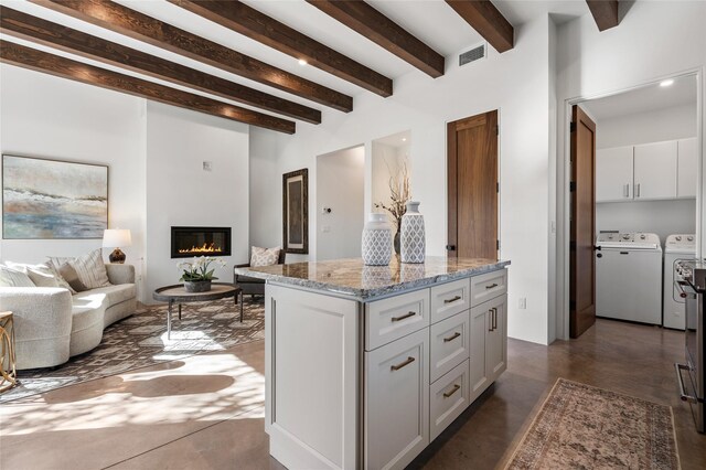 kitchen featuring a center island, beamed ceiling, washing machine and clothes dryer, white cabinetry, and light stone countertops