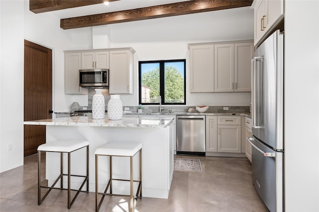 kitchen featuring a breakfast bar area, appliances with stainless steel finishes, a kitchen island, light stone counters, and beamed ceiling