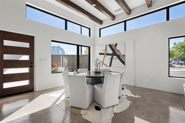 dining space with concrete floors, a high ceiling, and beamed ceiling