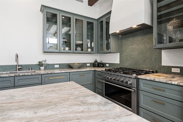 kitchen featuring premium range hood, stainless steel stove, light stone counters, and sink