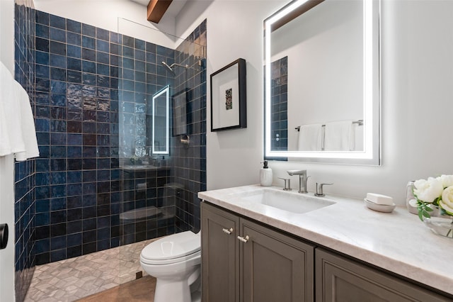 bathroom with toilet, tiled shower, and vanity