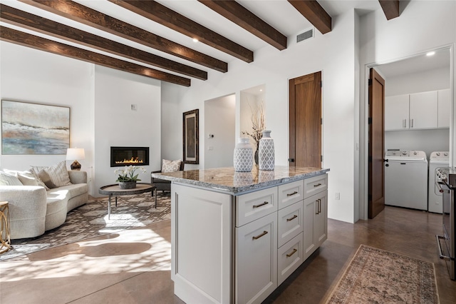 kitchen featuring white cabinetry, washing machine and clothes dryer, light stone countertops, a kitchen island, and beamed ceiling