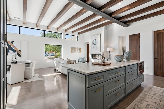 kitchen with beam ceiling, light stone countertops, gray cabinets, and a kitchen island