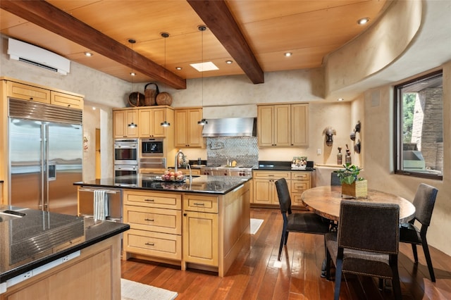 kitchen featuring appliances with stainless steel finishes, exhaust hood, decorative light fixtures, a center island with sink, and a wall mounted air conditioner