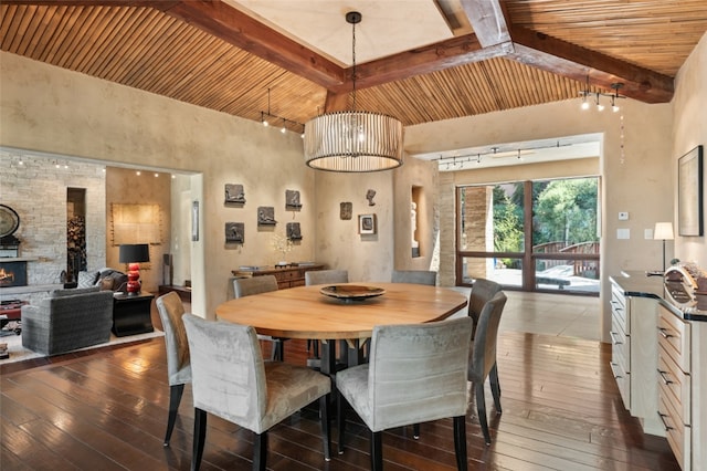 dining area with hardwood / wood-style flooring, rail lighting, beam ceiling, and a stone fireplace