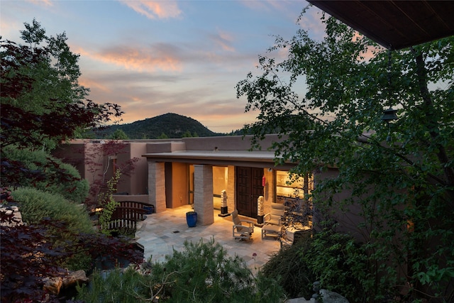 back house at dusk featuring a mountain view and a patio