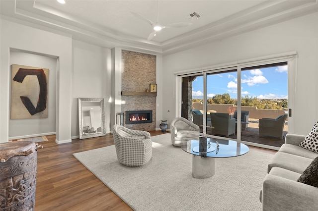 living room with a raised ceiling, ceiling fan, dark hardwood / wood-style flooring, and a large fireplace