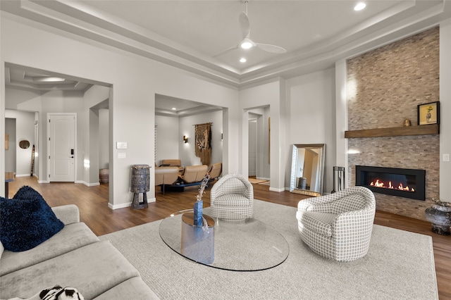 living room featuring hardwood / wood-style floors, a towering ceiling, a stone fireplace, ceiling fan, and a tray ceiling