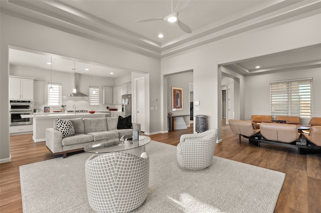 living room with ceiling fan, light hardwood / wood-style flooring, a tray ceiling, and sink