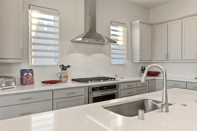 kitchen with gray cabinets, stainless steel appliances, sink, and wall chimney range hood