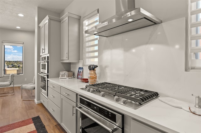 kitchen featuring light stone countertops, appliances with stainless steel finishes, wall chimney exhaust hood, and dark hardwood / wood-style flooring