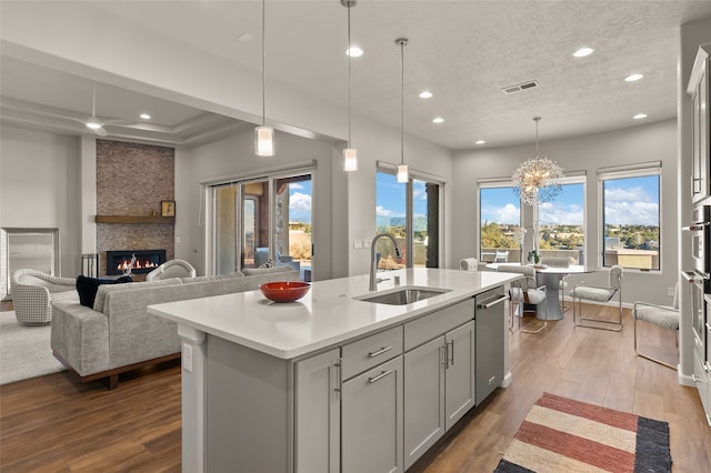 kitchen with a fireplace, hardwood / wood-style floors, sink, hanging light fixtures, and a kitchen island with sink