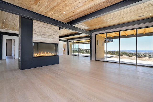 unfurnished living room featuring wood ceiling, a wall of windows, beam ceiling, a fireplace, and wood finished floors