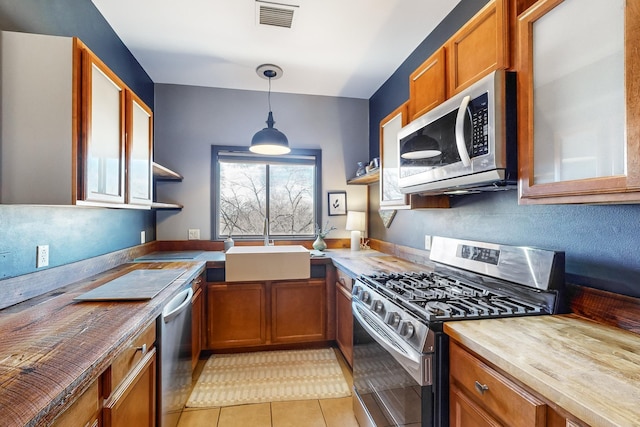 kitchen featuring decorative light fixtures, wooden counters, sink, appliances with stainless steel finishes, and light tile patterned floors