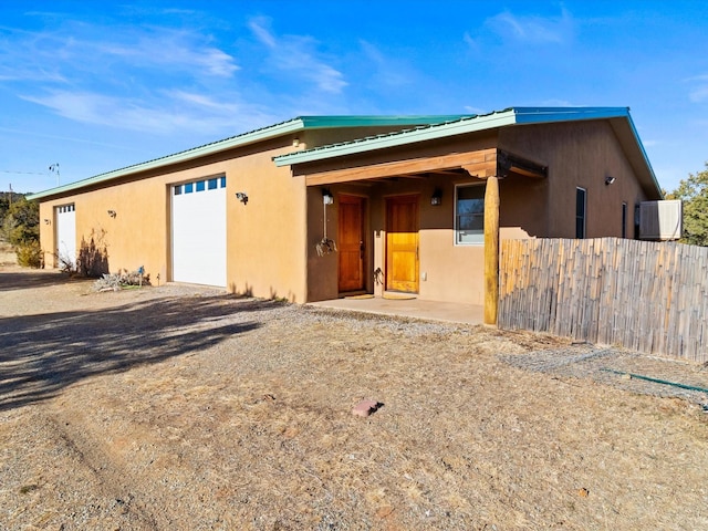 view of front facade featuring stucco siding, driveway, metal roof, and fence