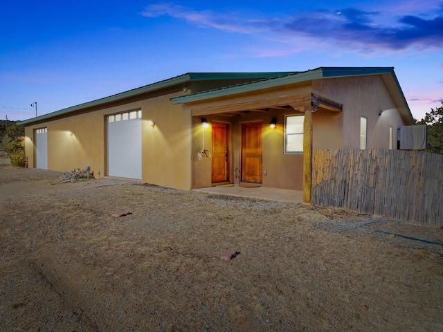 view of front of property featuring stucco siding, fence, a garage, and metal roof