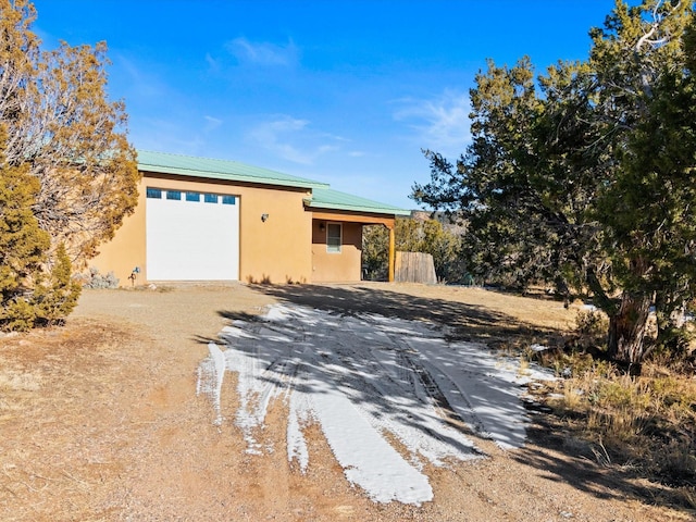 view of front facade with stucco siding, dirt driveway, and metal roof