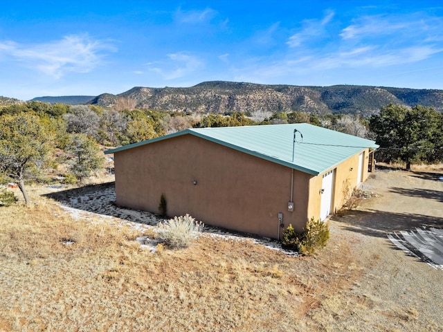 view of property exterior with metal roof, a garage, stucco siding, a mountain view, and an outdoor structure