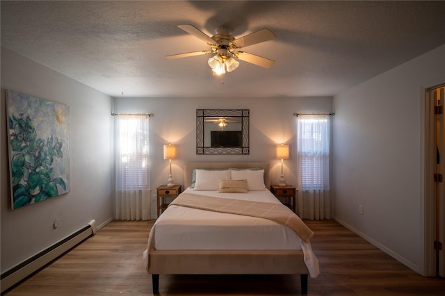 bedroom featuring a baseboard heating unit, ceiling fan, wood-type flooring, and multiple windows