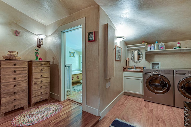 laundry area with sink, light wood-type flooring, washer and dryer, and cabinets