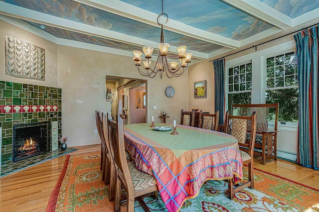 dining space with an inviting chandelier, hardwood / wood-style floors, a tiled fireplace, and beamed ceiling