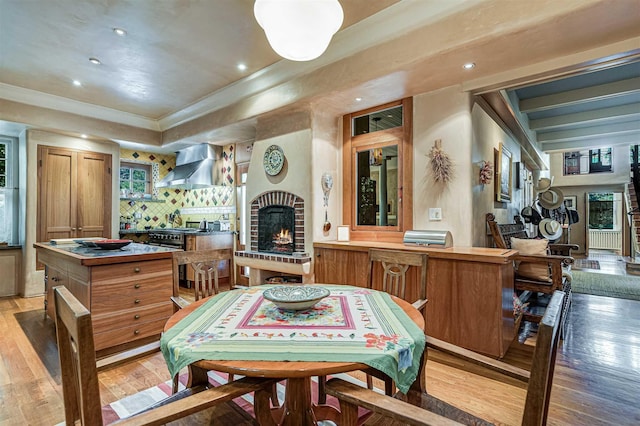 kitchen featuring light hardwood / wood-style floors, high end stove, decorative backsplash, a fireplace, and wall chimney range hood