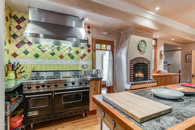 kitchen with double oven range, light hardwood / wood-style floors, island range hood, a brick fireplace, and backsplash