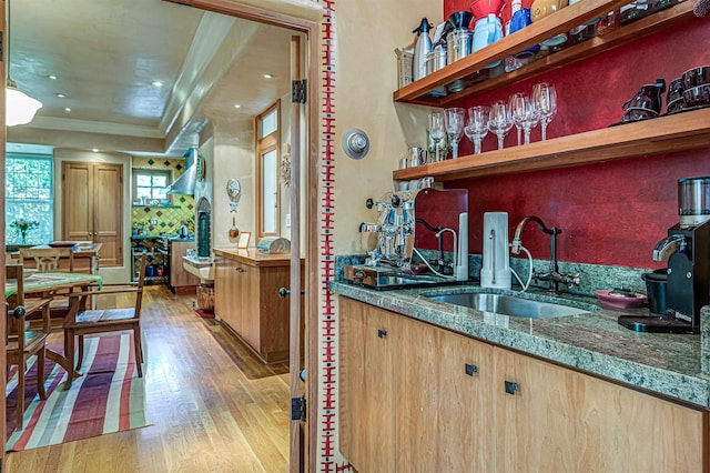 bar with sink, dark stone countertops, ornamental molding, and light hardwood / wood-style floors