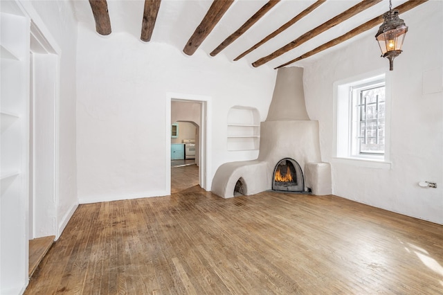 unfurnished living room featuring built in features, beamed ceiling, and hardwood / wood-style floors