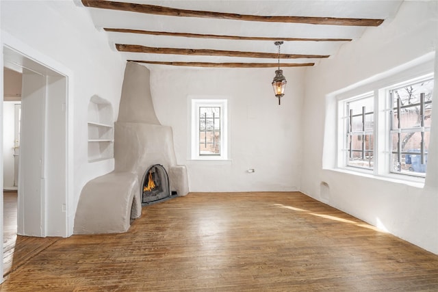 unfurnished living room featuring a fireplace, wood-type flooring, beam ceiling, and plenty of natural light