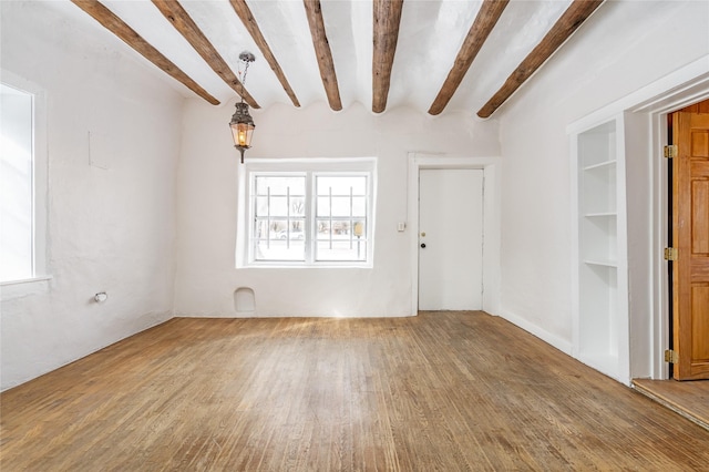 empty room featuring beam ceiling, built in shelves, and wood-type flooring