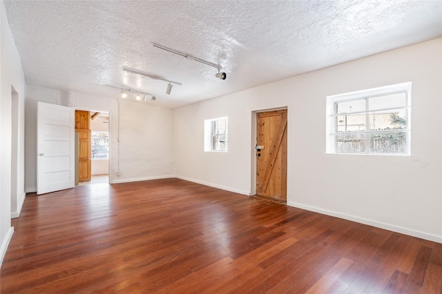 empty room with a textured ceiling, dark wood-type flooring, and a wealth of natural light