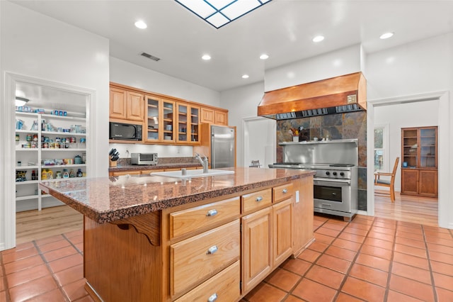 kitchen featuring premium range hood, a breakfast bar, sink, built in appliances, and a kitchen island with sink