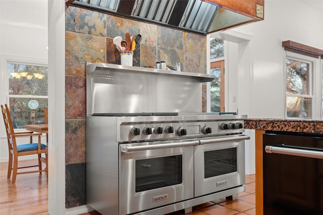 kitchen with luxury stove, light tile patterned floors, black dishwasher, and exhaust hood