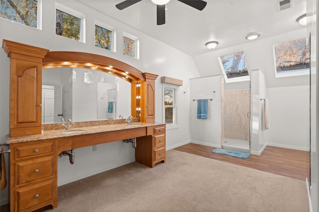 bathroom with ceiling fan, vaulted ceiling with skylight, walk in shower, and vanity