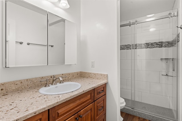 bathroom with toilet, a shower with shower door, hardwood / wood-style flooring, and vanity