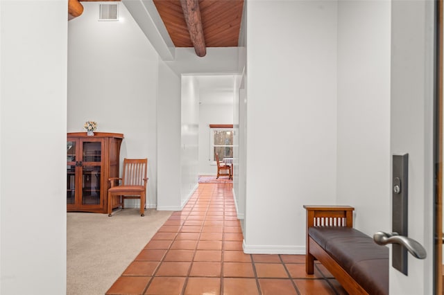 hallway with a towering ceiling, beamed ceiling, light carpet, and wood ceiling