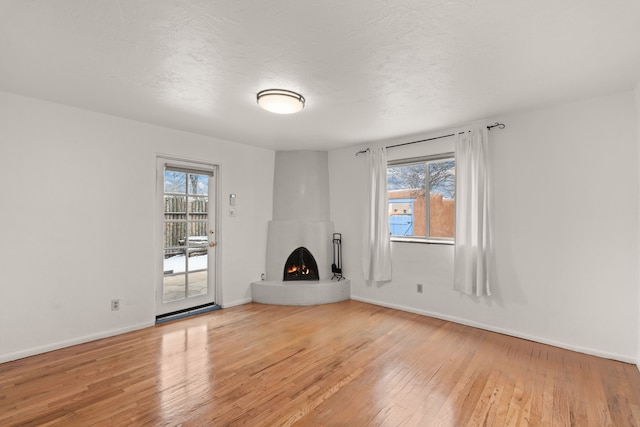 unfurnished living room featuring a large fireplace, a wealth of natural light, a textured ceiling, and light hardwood / wood-style flooring