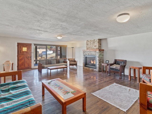 living room featuring a textured ceiling, a stone fireplace, and wood finished floors