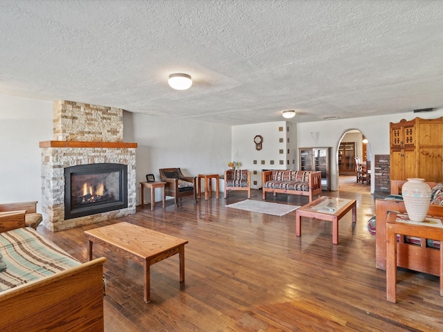 living area with arched walkways, a stone fireplace, a textured ceiling, and wood finished floors