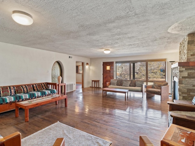 living room with visible vents, a textured ceiling, a stone fireplace, and wood finished floors