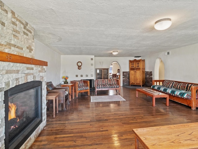 living area with arched walkways, visible vents, a stone fireplace, a textured ceiling, and hardwood / wood-style floors