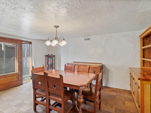 dining area with visible vents, a textured ceiling, and an inviting chandelier