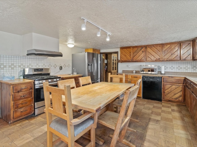 kitchen with light countertops, appliances with stainless steel finishes, wall chimney exhaust hood, brown cabinets, and backsplash