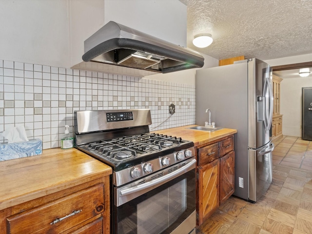 kitchen featuring a sink, stainless steel appliances, extractor fan, a textured ceiling, and wood counters